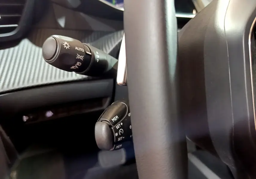 Gros plan sur la commande de régulateur de vitesse et éclairage derrière le volant cuir d'une Peugeot 208 jaune 2023.