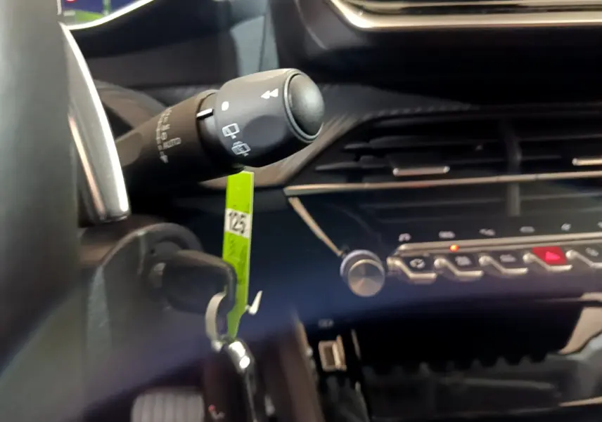 Détail intérieur du tableau de bord de la Peugeot 208 jaune 2023, avec commandes et clé insérée dans le contacteur.