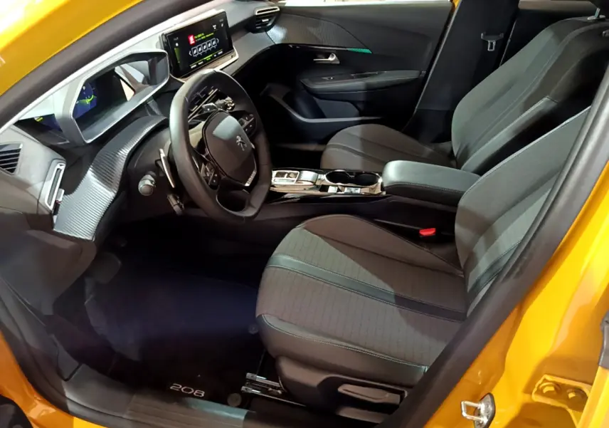 Vue intérieure côté conducteur de la Peugeot 208 jaune 2023, avec tableau de bord digital et sièges tissu gris.