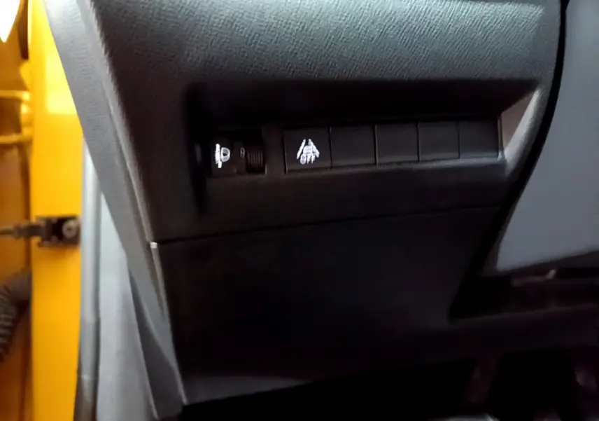 Détail des commandes d'aide à la conduite sur le côté gauche d'une Peugeot 208 jaune 2023.