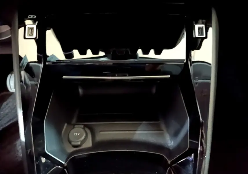Prise 12V en gros plan dans la console centrale noire de la Peugeot 208 jaune PureTech 2023