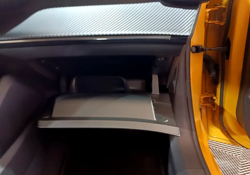 Gros plan sur la boîte à gants ouverte côté passager d'une Peugeot 208 jaune 2023, intérieur sombre et détails carbone.