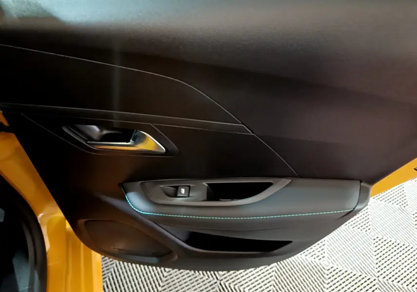 Vue rapprochée de la porte côté gauche jaune de la Peugeot 208 2023 avec poignée argentée et couture bleue.
