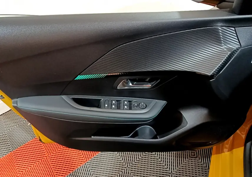 Vue rapprochée de la porte avant gauche noire avec insert effet carbone d'une Peugeot 208 jaune 2023.
