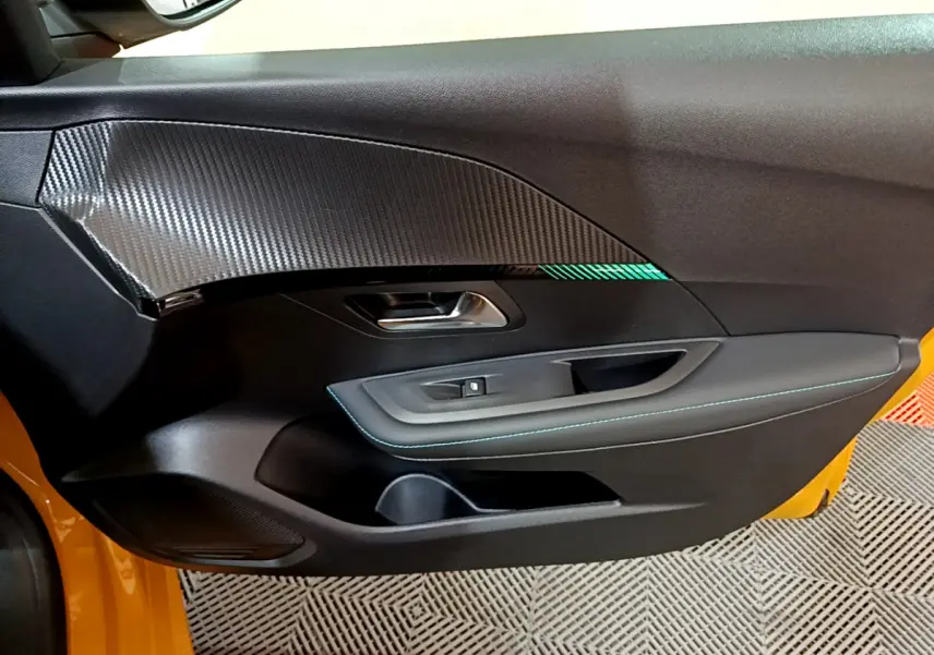 Vue rapprochée de la porte côté gauche jaune de la Peugeot 208 avec insert carbone et surpiqûres bleues.