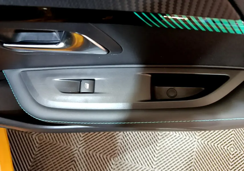 Gros plan sur la poignée intérieure et le bouton de lève-vitre côté gauche de la porte d'une Peugeot 208 jaune.