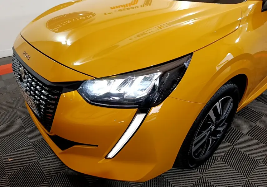 Gros plan sur l'avant droit d'une Peugeot 208 jaune 2023 avec phares LED allumés et calandre noire texturée