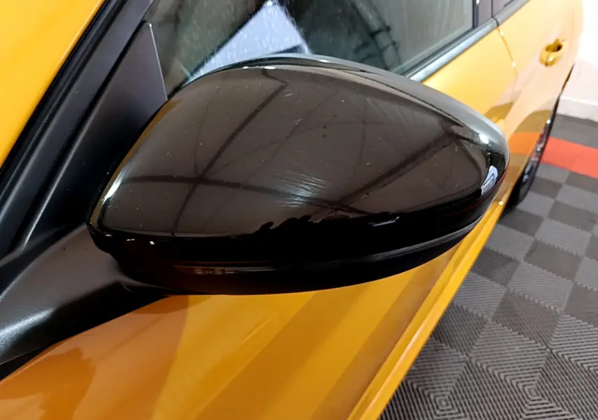 Rétroviseur noir côté gauche d'une Peugeot 208 jaune vue en gros plan sur fond intérieur.