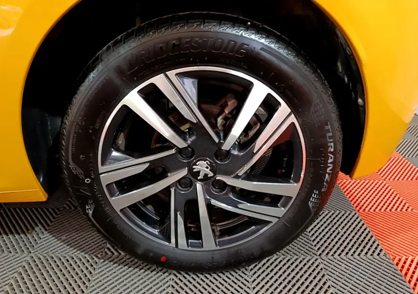 Gros plan sur la roue avant gauche de la Peugeot 208 jaune avec jante alliage noire et argentée distinctive.