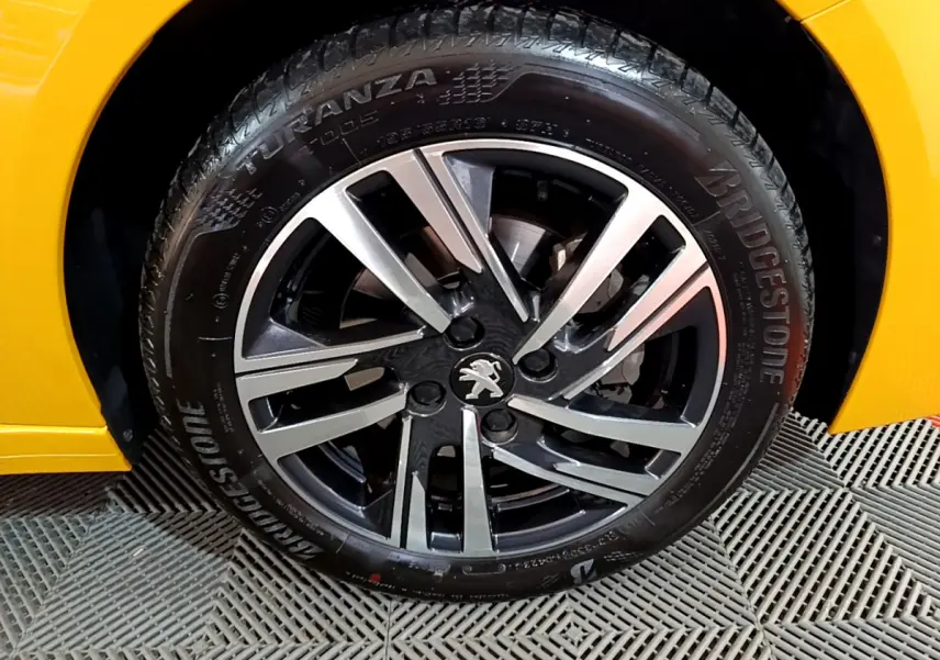 Gros plan sur la roue avant droite de la Peugeot 208 jaune 2023 avec jante alliage bicolore et pneu Bridgestone.