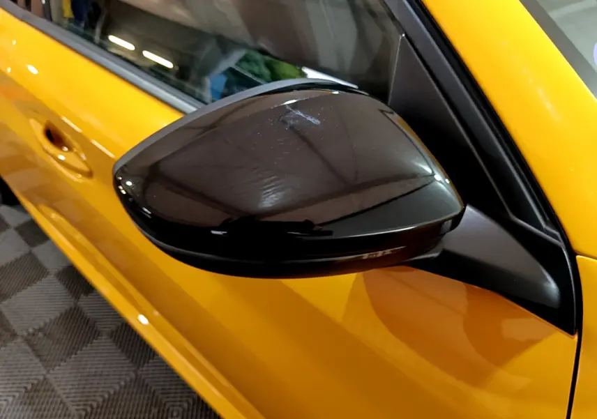 Rétroviseur noir brillant côté conducteur d'une Peugeot 208 jaune vue de près sur porte avant.