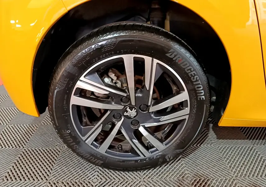 Gros plan sur la roue avant gauche d'une Peugeot 208 jaune 2023 avec jante alliage et pneu Bridgestone.