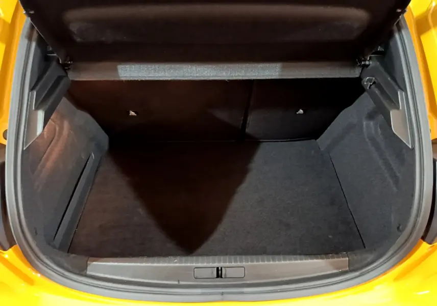 Coffre ouvert vu de l'arrière d'une Peugeot 208 jaune 2023, espace de chargement vide et tapis noir.