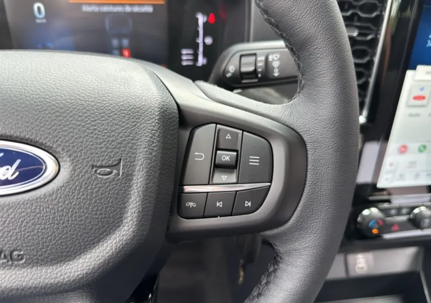 Gros plan sur le volant en cuir du Ford Ranger gris carbone 2025, avec commandes intégrées et tableau de bord numérique visible.