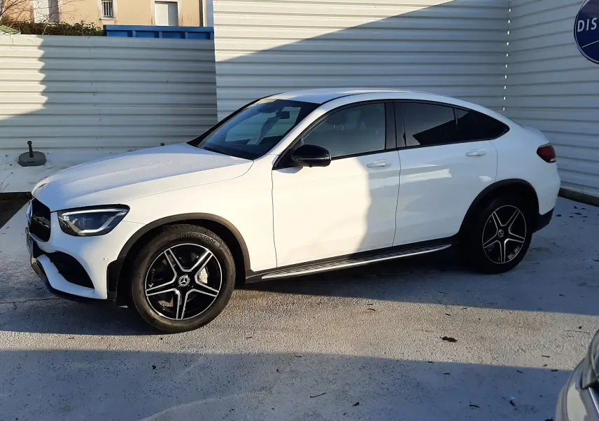 Vue 3/4 avant droite d’un Mercedes GLC Coupé 300 4MATIC AMG Line blanc avec jantes AMG et calandre étoilée.