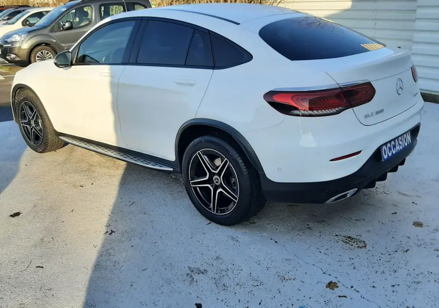 Vue 3/4 arrière côté droit d'un Mercedes GLC Coupé 300 4MATIC AMG Line blanc avec jantes noires et toit panoramique.