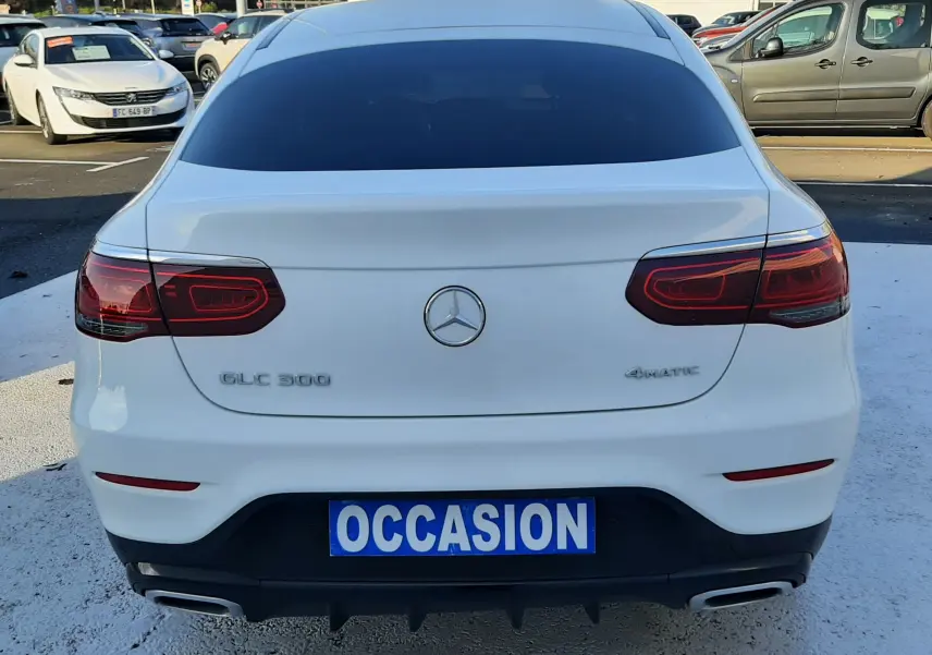 Vue 3/4 arrière droite d’un Mercedes GLC Coupé blanc 2019 avec jantes AMG noires et vitres teintées.