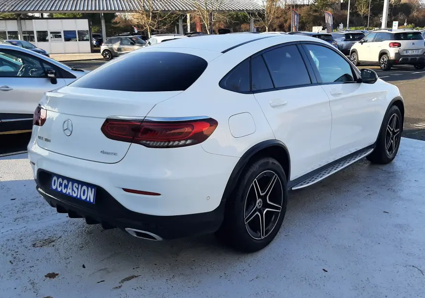 Vue 3/4 arrière droite d’un Mercedes GLC Coupé 300 4MATIC blanc avec feux LED et jantes noires, sur parking extérieur.