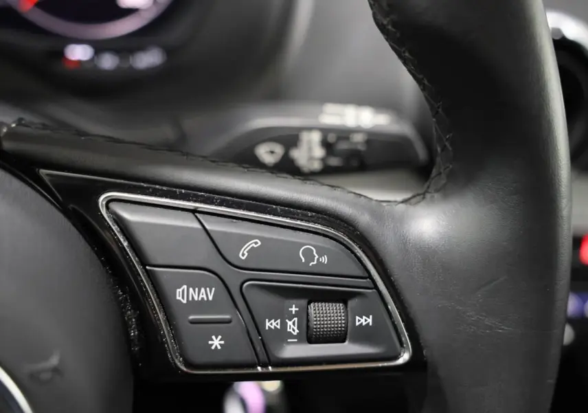 Gros plan sur les commandes multifonctions du volant en cuir noir de l’Audi Q2 TFSI 110 gris, avec boutons de navigation et volume.
