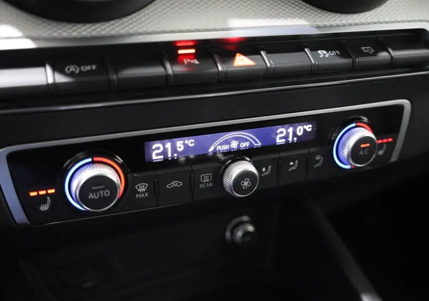 Gros plan sur la console de climatisation de l’Audi Q2 gris, avec réglages digitaux et boutons rétroéclairés.