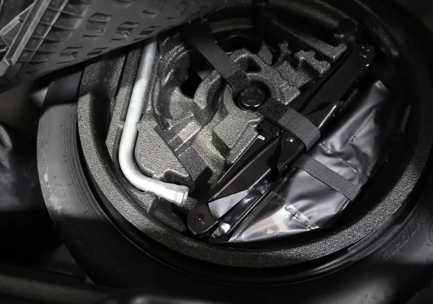 Vue rapprochée de la roue de secours et du kit de réparation dans le coffre d'un Audi Q2 gris 2023.