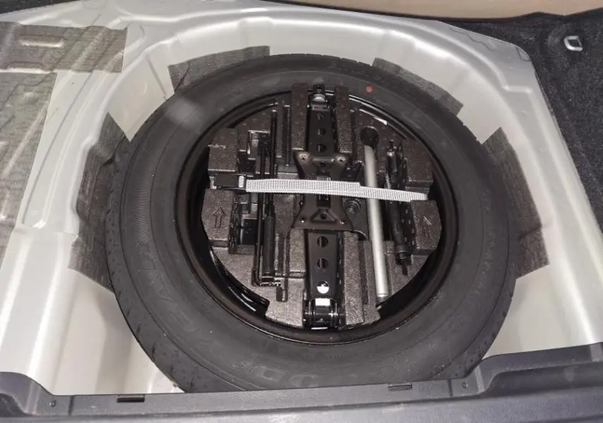 Vue plongeante sur la roue de secours noire et ses outils dans le coffre d’un Skoda Kamiq gris 2023.