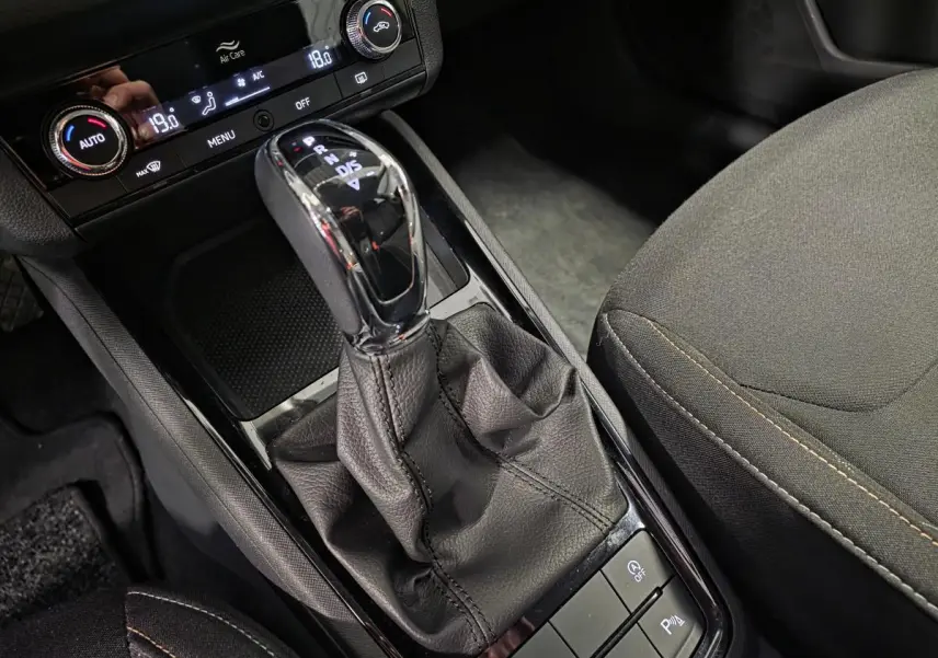 Gros plan sur le levier de vitesses automatique noir et la console centrale du Skoda Kamiq gris, avec commandes de climatisation visibles.