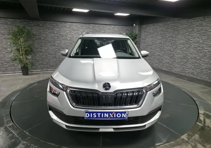 Vue avant d'un Skoda Kamiq gris métallisé avec calandre noire et plaque Distinxion en intérieur showroom.
