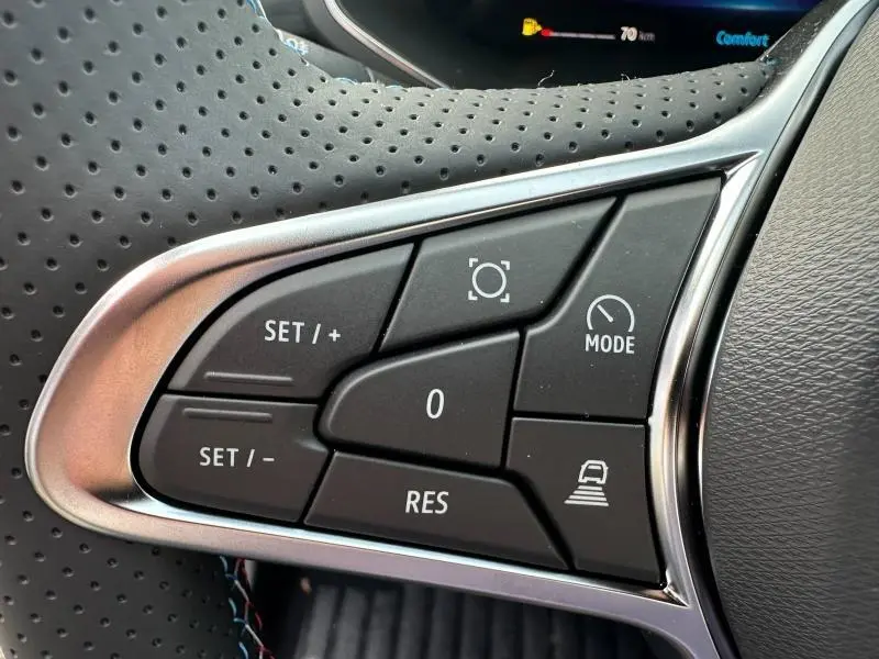 Gros plan sur les commandes au volant perforé du Renault Captur 2026 gris Rafale/Noir Étoilé, boutons de régulateur et mode.