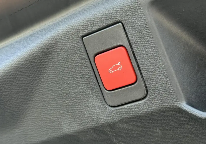 Gros plan sur le bouton rouge d'ouverture électrique du hayon dans l'habitacle du Peugeot 5008 noir Perla.