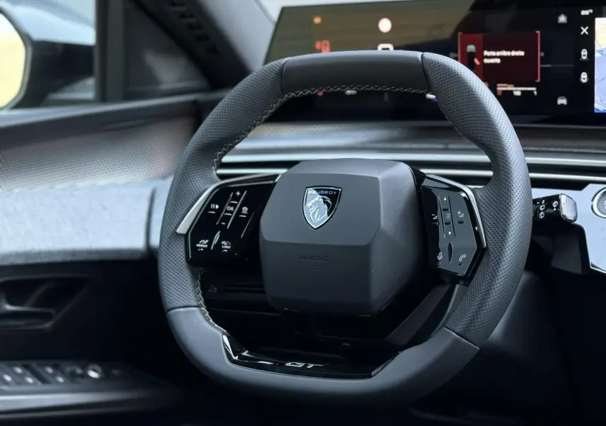 Volant compact Peugeot 5008 GT noir perforé avec commandes intégrées, vue rapprochée depuis le siège conducteur.