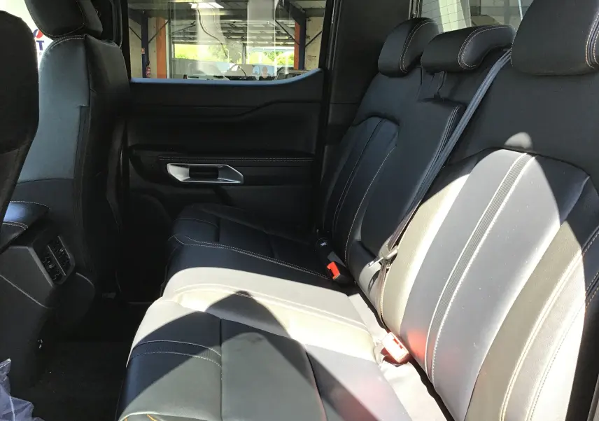 Vue latérale intérieure des sièges arrière en cuir noir avec surpiqûres contrastantes du Ford Ranger Double Cabine gris carbone 2025.
