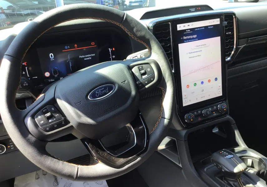 Vue intérieure du Ford Ranger Wildtrak 2025 montrant le volant cuir noir avec surpiqûres orange et l'écran tactile central vertical.