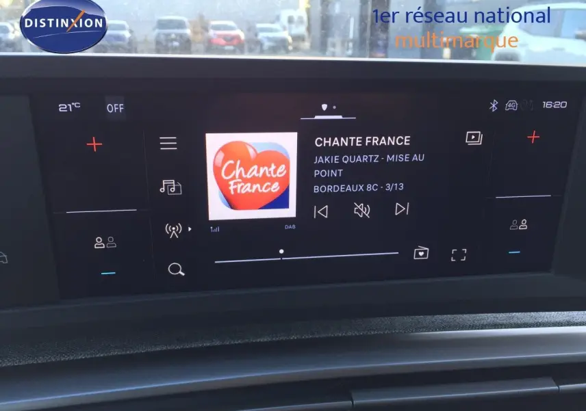 Écran tactile central du tableau de bord du Peugeot 5008 blanc, affichant la radio Chante France en extérieur urbain.