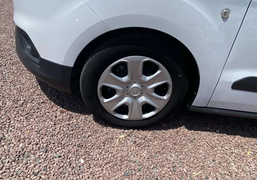 Gros plan sur la roue avant gauche avec enjoliveur argenté du Ford Tourneo Courier blanc stationné sur gravier.