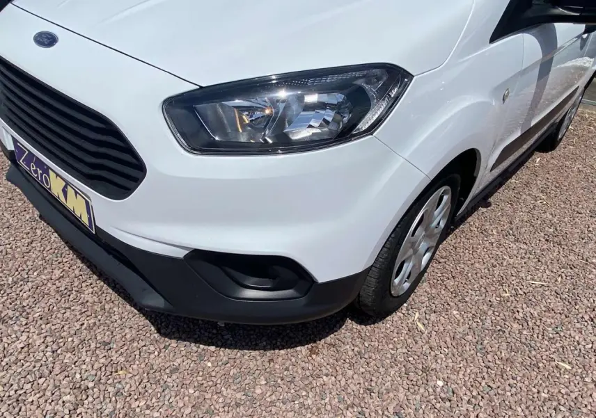 Vue 3/4 avant droit d'un Ford Tourneo Courier blanc avec enjoliveurs cache moyeu sur un sol gravillonné.