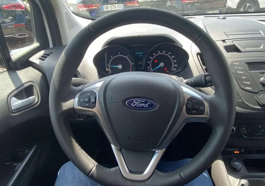 Vue intérieure centrée sur le volant cuir Ford d'un Tourneo Courier blanc, avec tableau de bord et commandes au volant visibles.