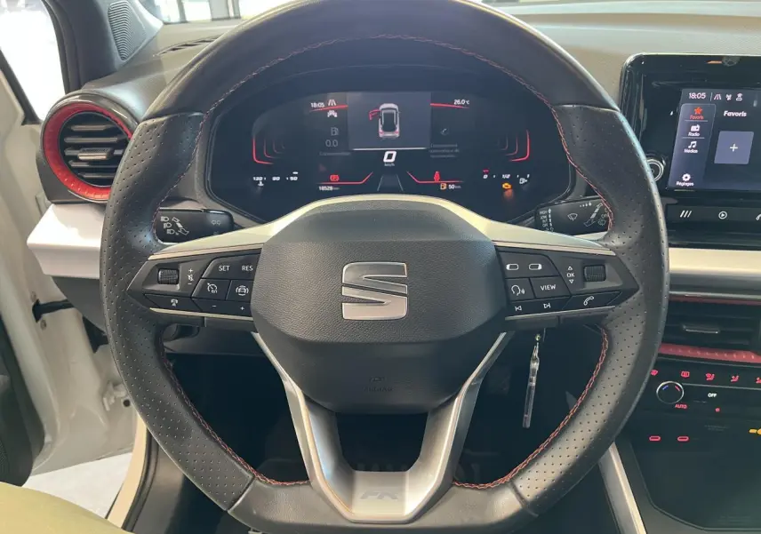 Vue rapprochée du volant sport cuir perforé avec surpiqûres rouges et tableau de bord digital du SEAT Arona blanc Nevada.