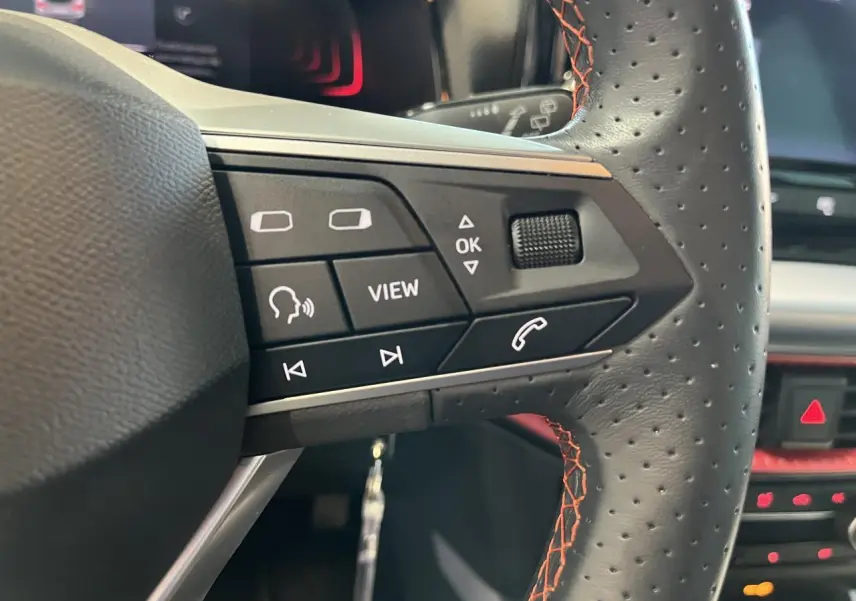 Gros plan sur les commandes du volant sport cuir perforé avec surpiqûres rouges du SEAT Arona blanc Nevada 2024.