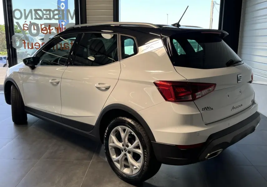 SEAT Arona blanc Nevada vu de 3/4 arrière droit avec toit noir et jantes alliage 16 pouces en showroom.