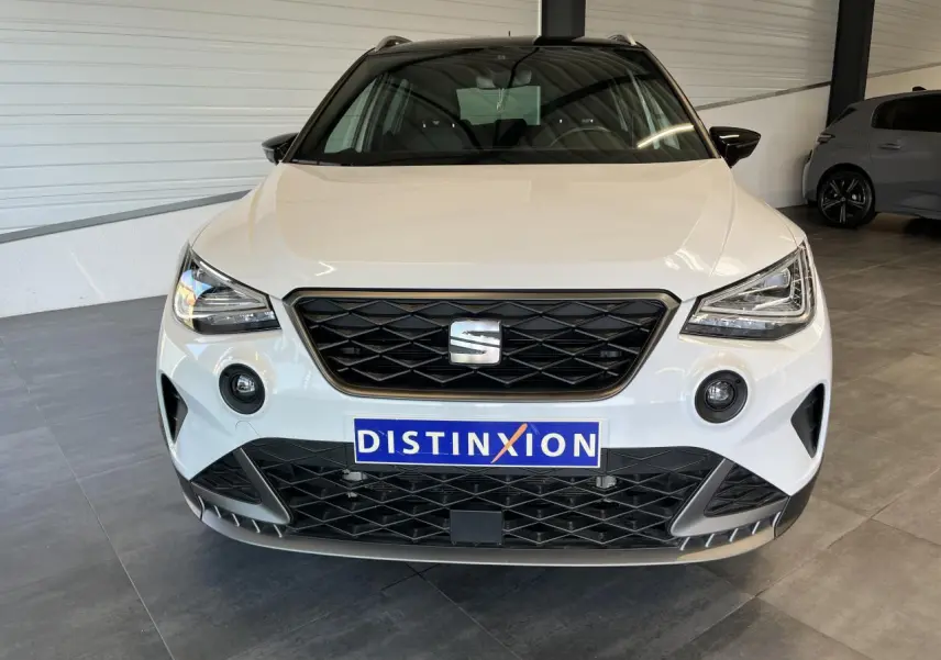 Vue frontale d'un SEAT Arona blanc Nevada avec calandre noire et projecteurs EcoLED dans un showroom.