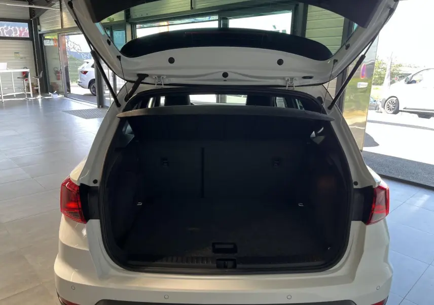 Coffre ouvert vu de l'arrière d'un SEAT Arona blanc Nevada 2024 dans un showroom lumineux.