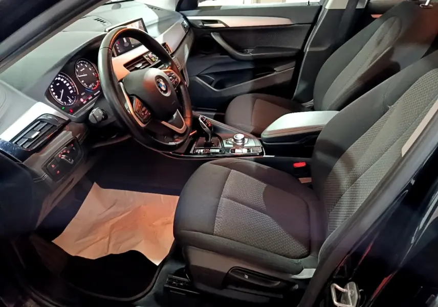 Vue intérieure côté conducteur de la BMW X2 sDrive18i Lounge 2023, sièges noirs et volant cuir multifonctions.