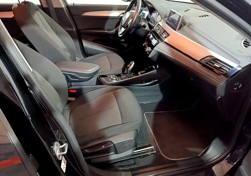 Vue intérieure côté conducteur de la BMW X2 sDrive18i Lounge noire, avec tableau de bord et sièges en tissu gris.