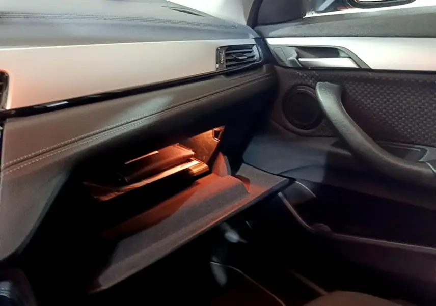 Intérieur BMW X2 sDrive18i Lounge 2023, vue côté passager sur boîte à gants ouverte avec éclairage ambiant noir.