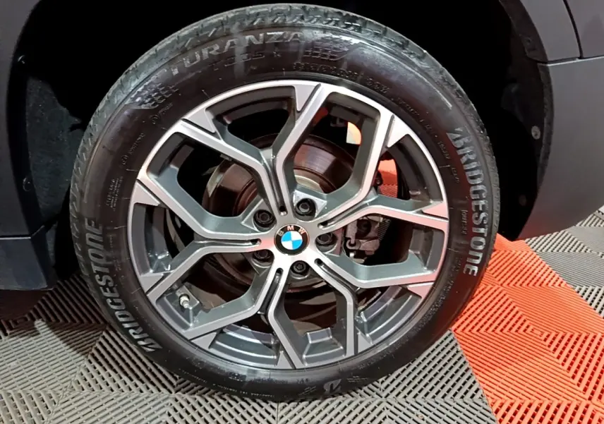 Gros plan sur la roue avant droite d’un BMW X2 noir avec jante alliage à design moderne et logo BMW central.