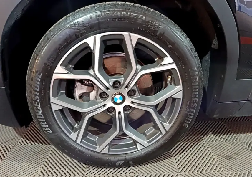 Gros plan sur la roue avant droite d’une BMW X2 noire avec jante alliage et pneu Bridgestone Turanza.