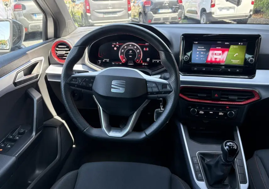 Intérieur de la SEAT Arona 2024 vu du siège conducteur, volant sport cuir, détails rouges autour des aérateurs et console centrale.