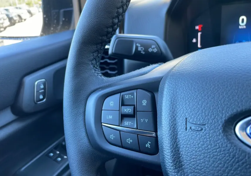 Gros plan sur le volant noir du Ford Ranger 2025, montrant les commandes de régulateur et audio côté gauche.