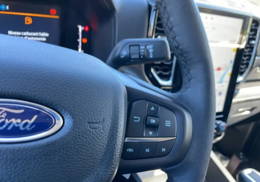 Gros plan sur le volant en cuir noir du Ford Ranger 2025, avec commandes intégrées et tableau de bord numérique en arrière-plan.